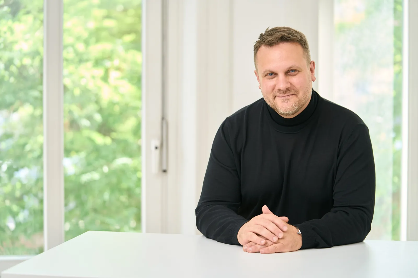Kartellrecht für Unternehmen – Slopek Rechtsanwälte Rechtsanwalt Dr. David Slopek, LL.M., lächelnd am Besprechungstisch der Kanzlei – Beratung im Kartellrecht bei Slopek Rechtsanwälte